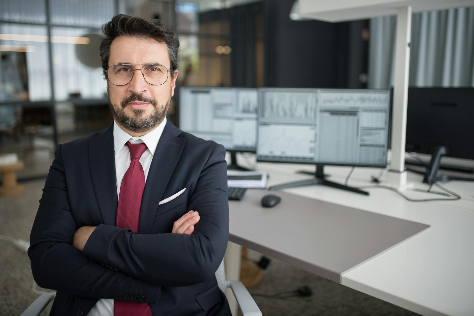 Business professional in corporate attire with arms crossed in a modern office space.